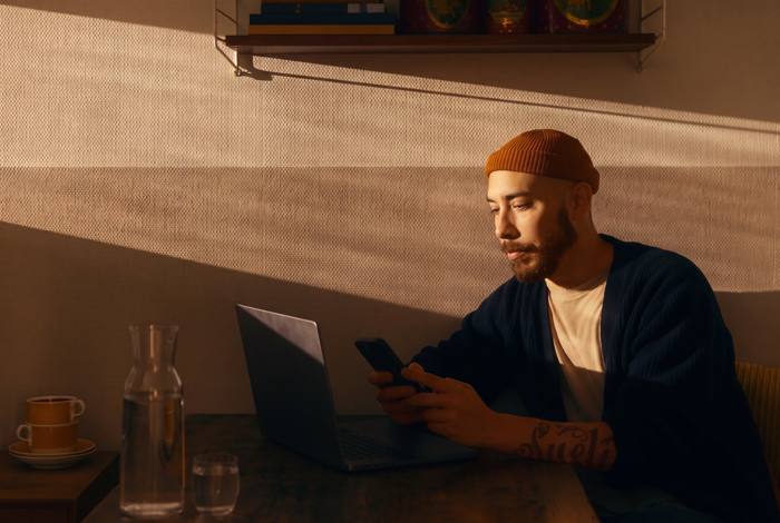Daniel at a desk in the evening, phone in hand, laptop open